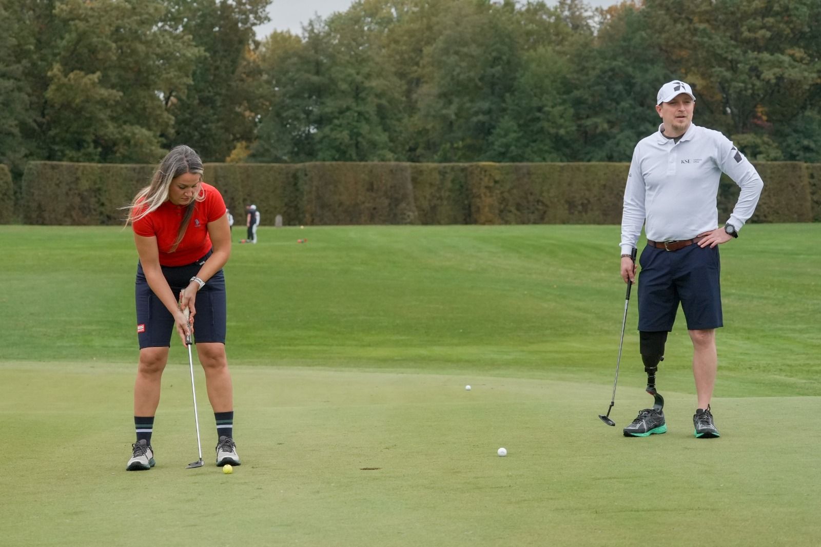 A player on a leg prosthesis waits on the putting green at Golf Brdo while another player putts